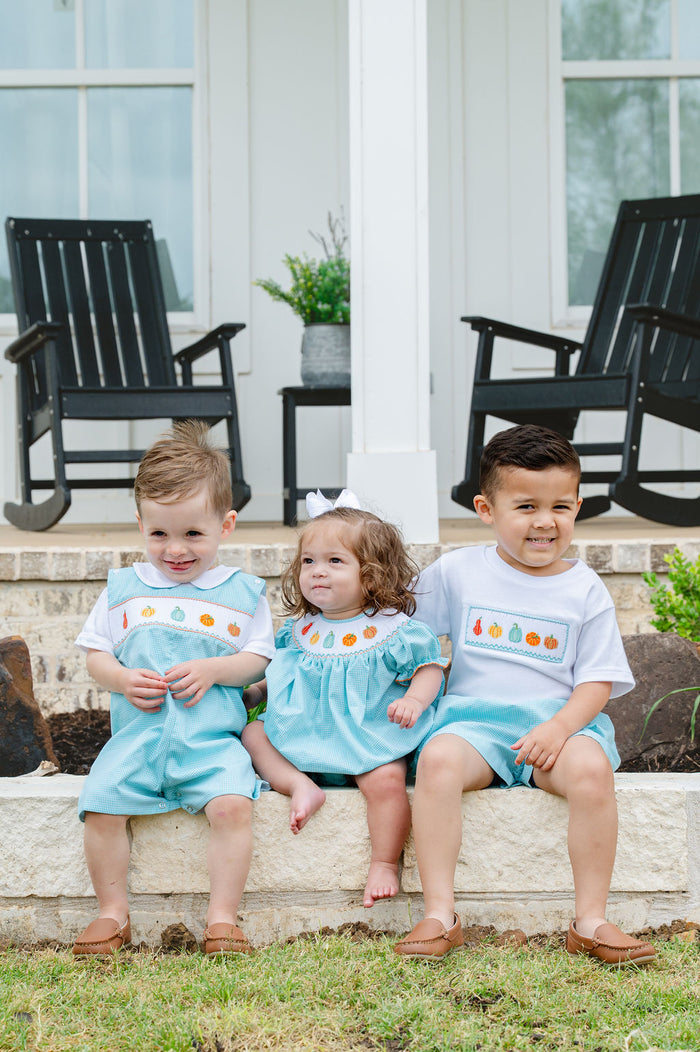 Three children sitting on steps wearing matching Smocked Fall Gourds outfits outdoors