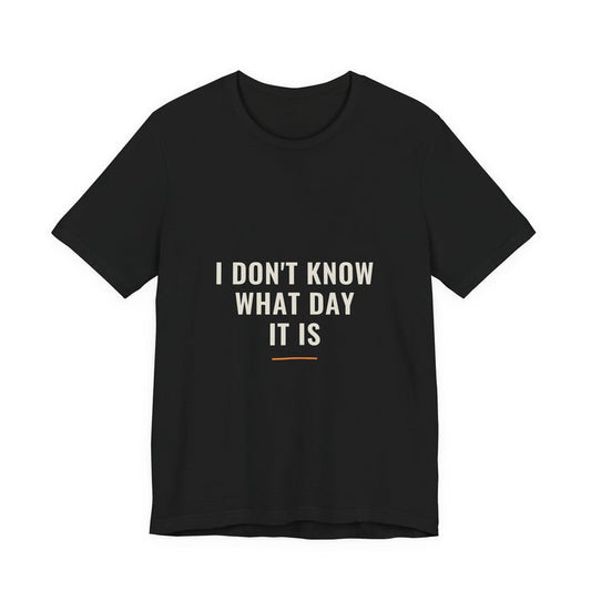 I DON'T KNOW WHAT DAY IT IS set in three cream lines above a short orange rule, printed on a black unisex t-shirt.