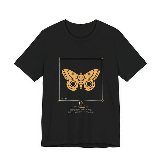 A golden-yellow io moth with two dark ringed eyespots, drawn as a specimen plate inside a thin bracket frame with a 50 mm scale bar, labelled IO / Automeris io, printed on a black unisex t-shirt.