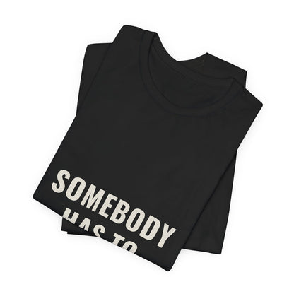 Black Somebody Has To t-shirt folded to show the front print at an angle.