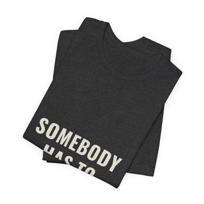 Dark grey heather Somebody Has To t-shirt folded to show the front print at an angle.