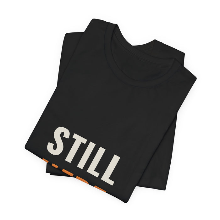 Black Still Here t-shirt folded to show the front print at an angle.