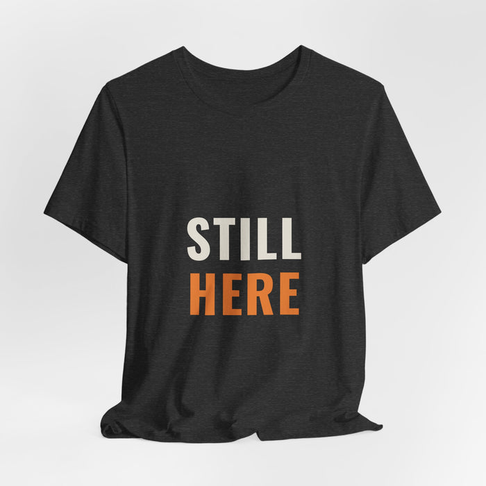 Dark grey heather Still Here t-shirt shown draped, front print visible.