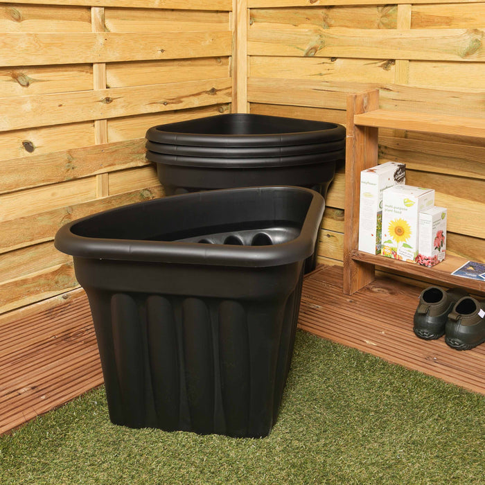 Two black plastic planters against a wooden wall with gardening supplies.